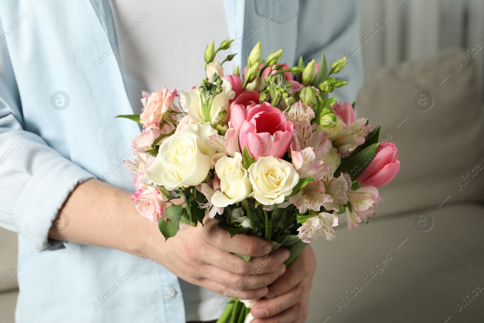 Photo of Man holding bouquet of beautiful flowers indoors, closeup