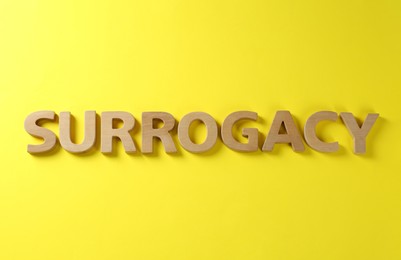 Word Surrogacy made of wooden letters on yellow background, flat lay