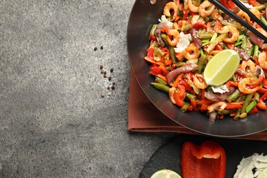 Photo of Shrimp stir fry with vegetables in wok and chopsticks on grey table, flat lay. Space for text