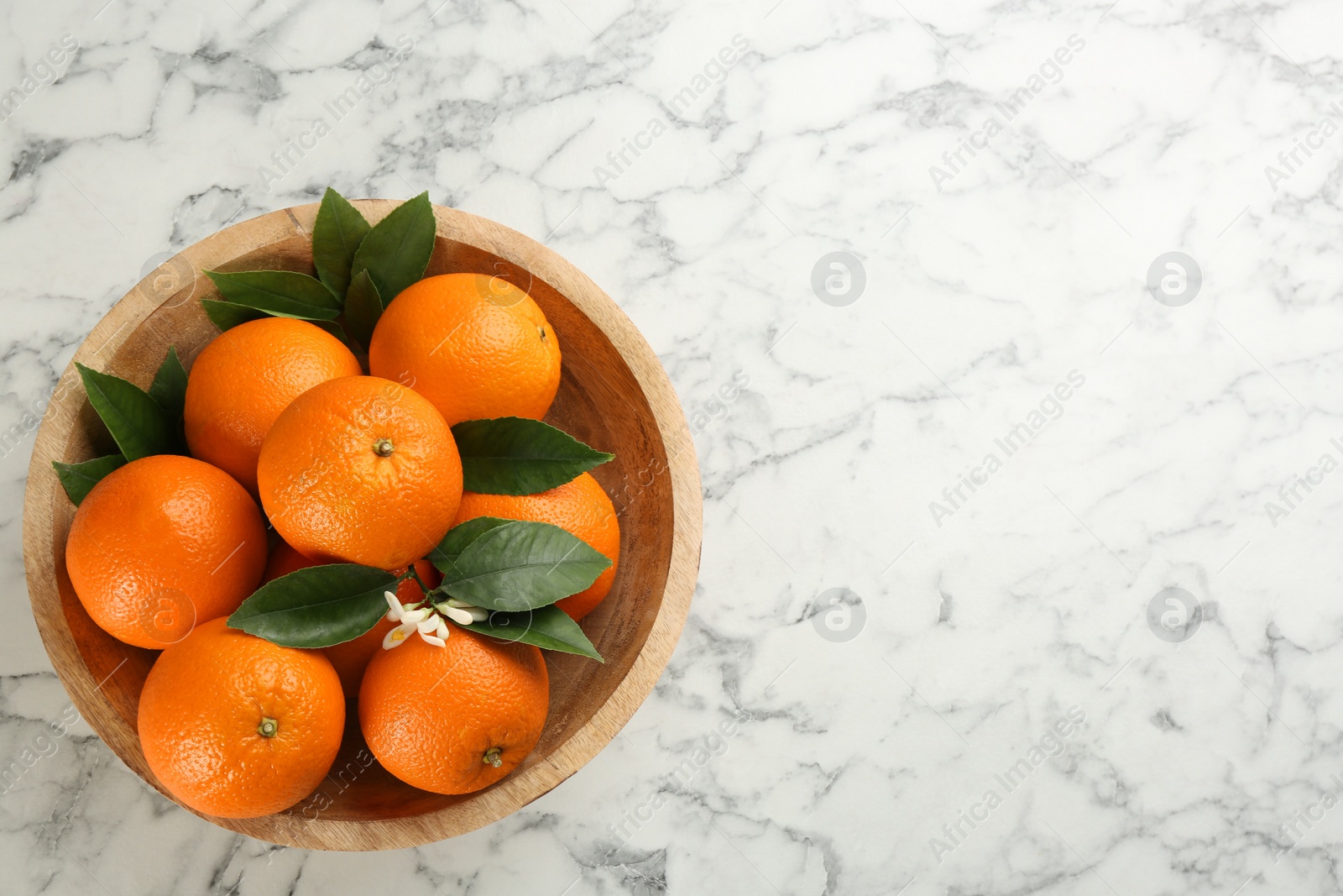 Photo of Delicious ripe oranges in bowl on white marble table, top view. Space for text