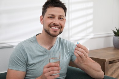 Photo of Man with glass of water taking pill at home
