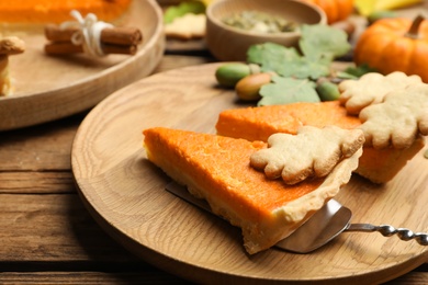 Photo of Slices of delicious homemade pumpkin pie on wooden plate, closeup