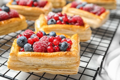 Cooling rack and fresh delicious puff pastry with sweet berries on white marble table, closeup