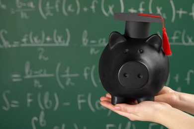 Photo of Woman holding piggy bank and graduation cap against greenboard, closeup with space for text. Scholarship concept