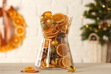 Photo of Glass vase with dry orange slices, cones and Christmas tree balls on white wooden table. Festive decor