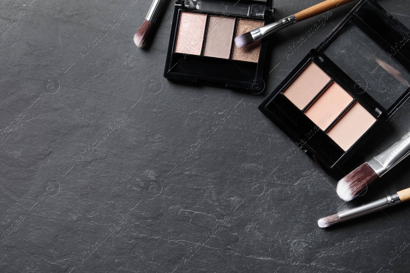 Photo of Beautiful eye shadow palettes and brushes on dark grey textured table, flat lay. Space for text