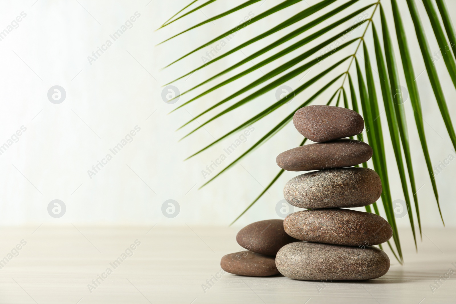 Photo of Stack of spa stones and palm leaf on table against white background, space for text