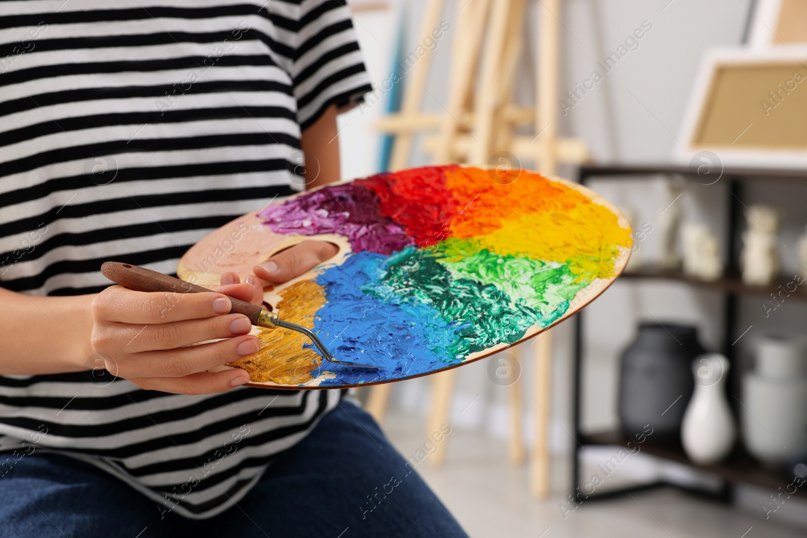 Photo of Young woman mixing paints on palette in studio, closeup