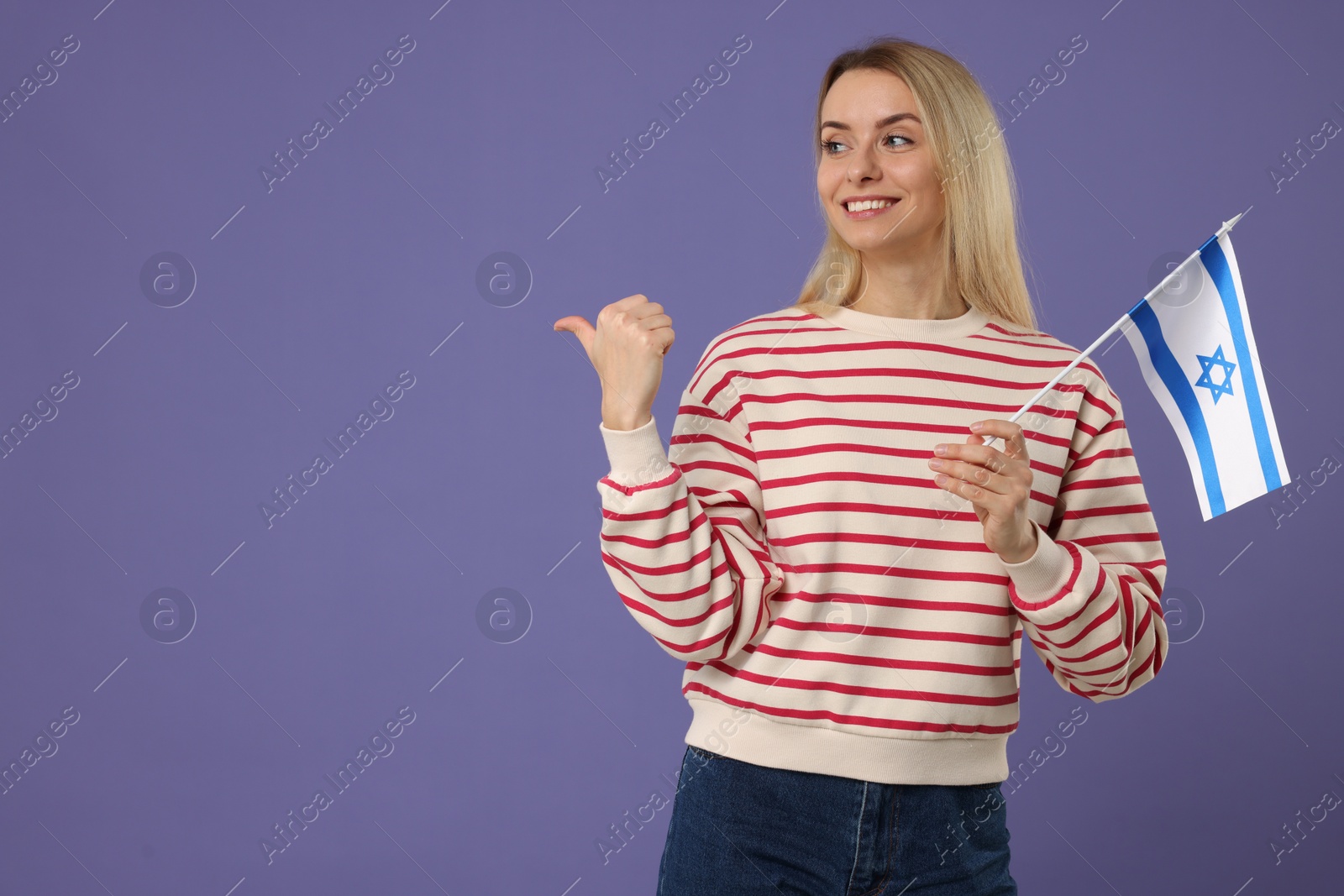 Photo of Happy woman with flag of Israel pointing at something on violet background, space for text
