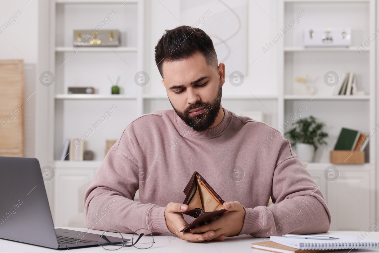 Photo of Upset man with empty wallet at table indoors