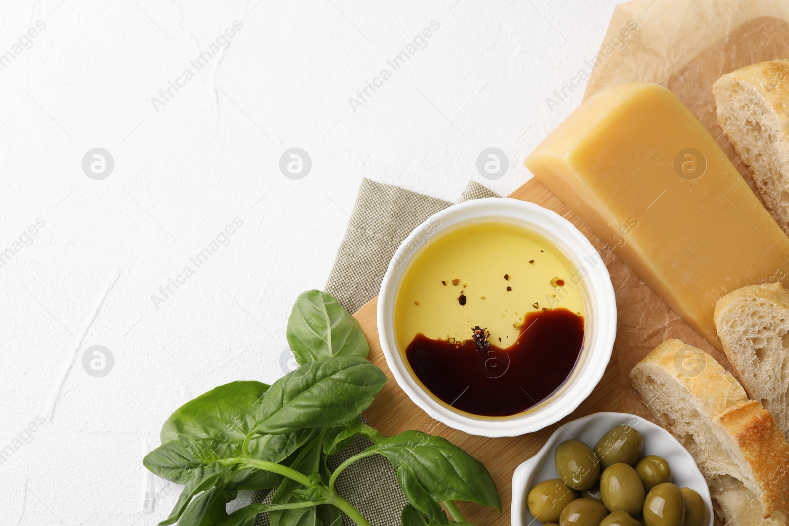 Photo of Bowl of organic balsamic vinegar with oil, basil, bread, cheese and olives on white table, flat lay. Space for text