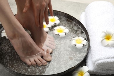 Photo of Woman soaking her feet in bowl with water and flowers on floor, closeup. Spa treatment