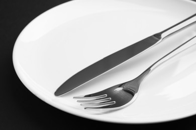 Photo of Clean plate, fork and knife on black table, closeup