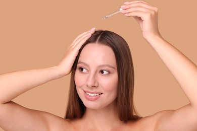 Beautiful woman applying serum onto hair on beige background