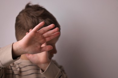 Photo of Child abuse. Boy doing stop gesture on light grey background, selective focus and space for text