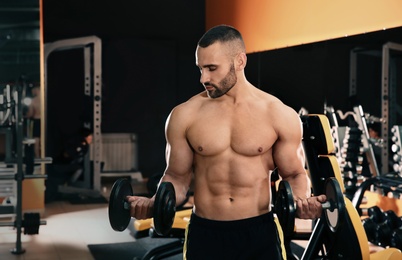 Strong young man lifting dumbbells in gym