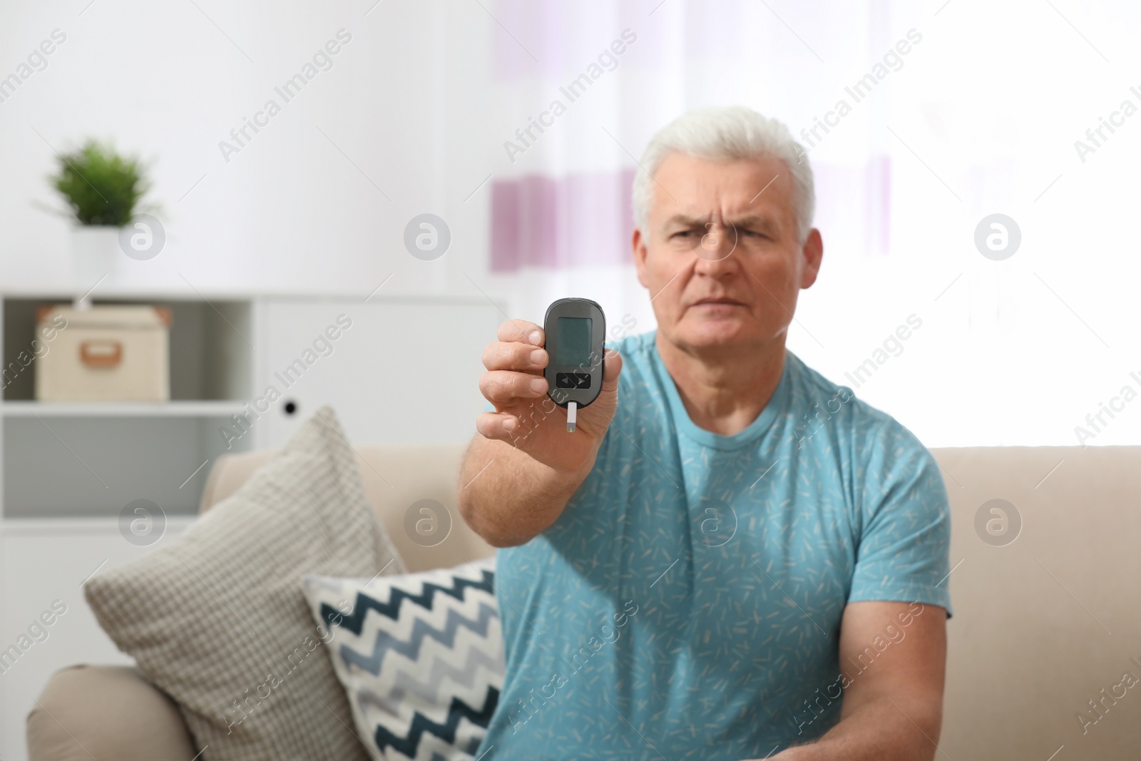 Photo of Senior man holding digital glucometer at home. Diabetes control