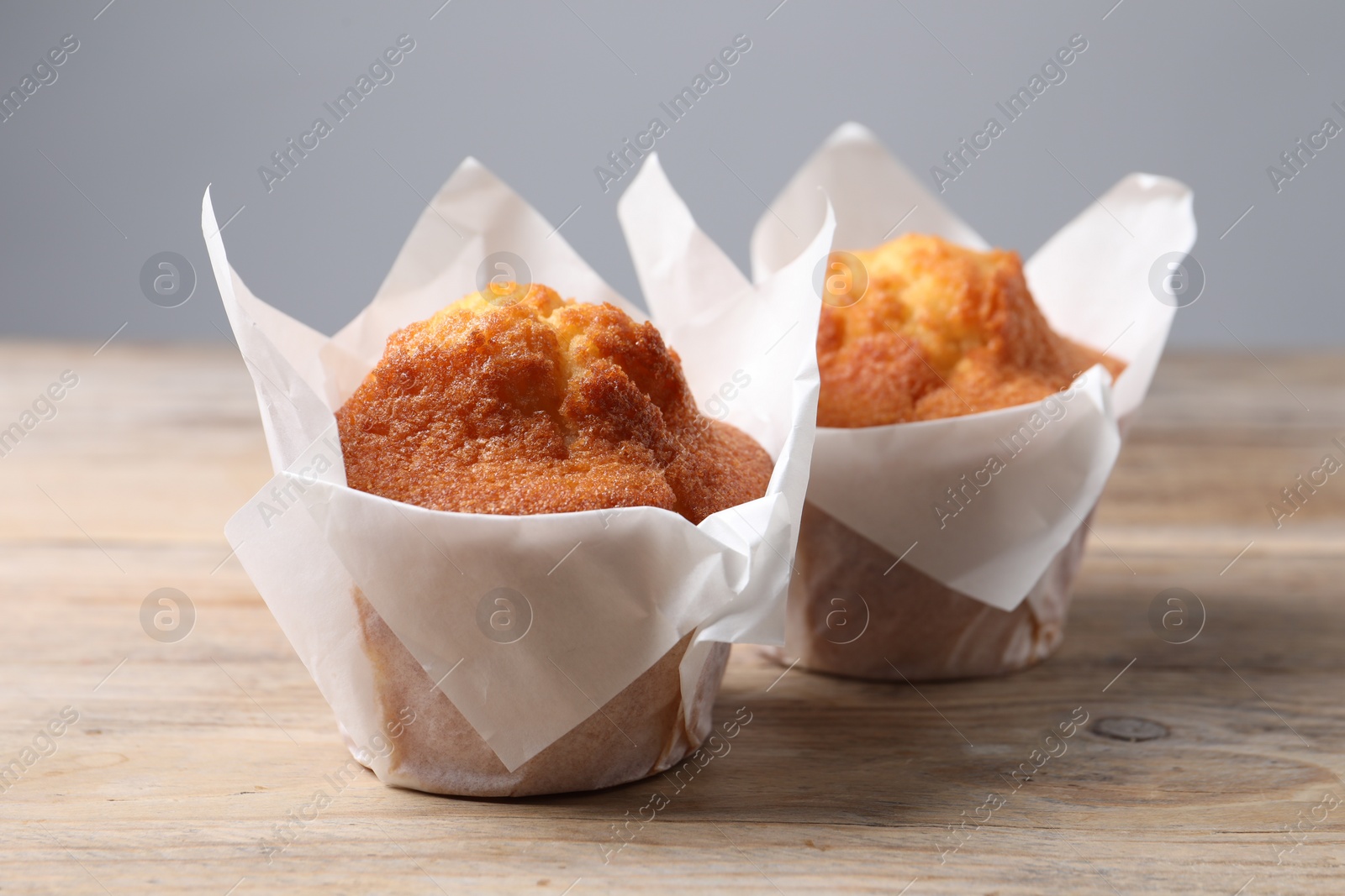 Photo of Delicious sweet muffins on wooden table against grey background, closeup