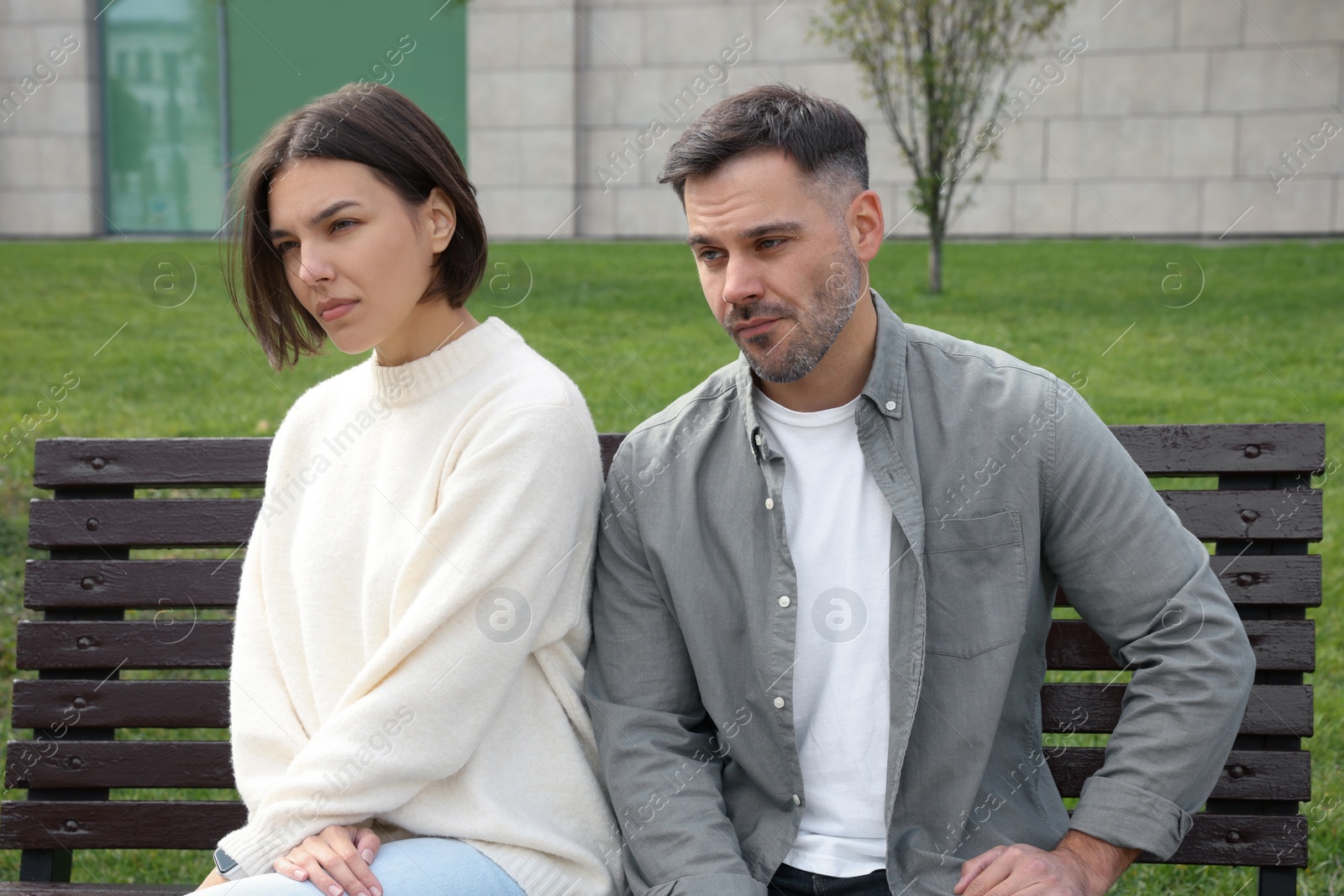 Photo of Unhappy couple sitting on bench outdoors. Relationship problems