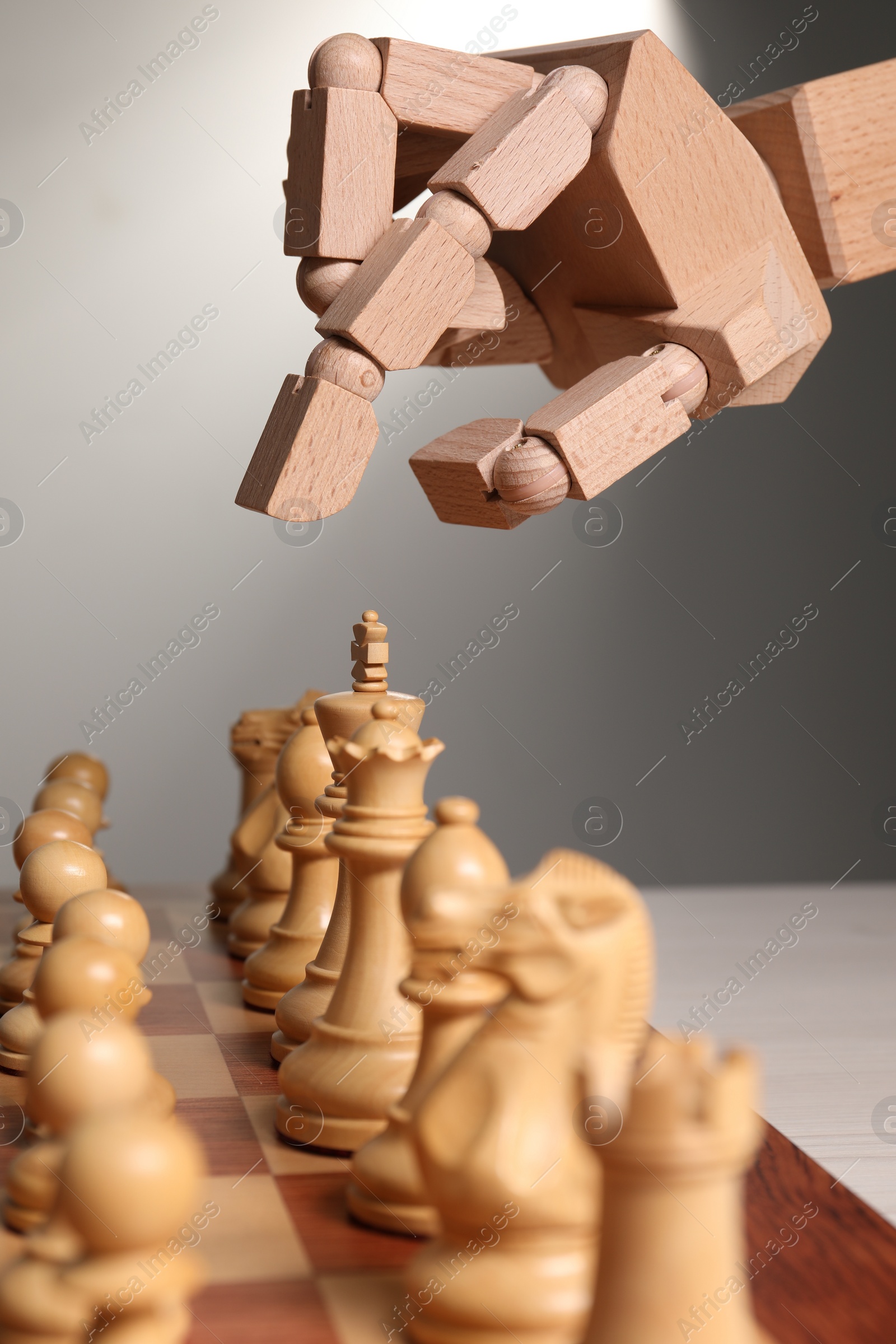 Photo of Robot playing chess against light grey background, closeup. Wooden hand representing artificial intelligence