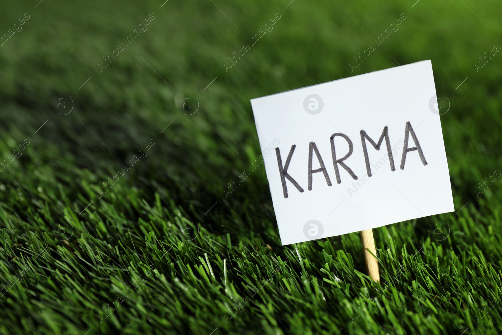 Photo of Sign with word Karma on green grass, closeup. Space for text