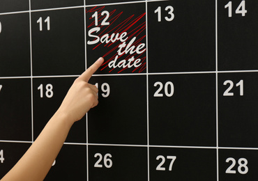 Image of Woman pointing on board calendar with phrase SAVE THE DATE, closeup
