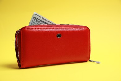 Photo of Stylish red leather purse with dollar banknotes on yellow background