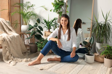 Photo of Happy young woman sitting near mirror and different houseplants in room