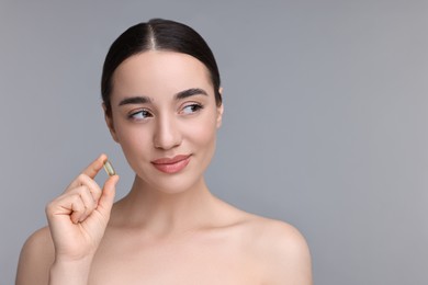 Beautiful young woman with vitamin pill on grey background