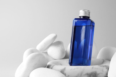 Photo of Bottle of cosmetic product and stones on light grey background. Space for text