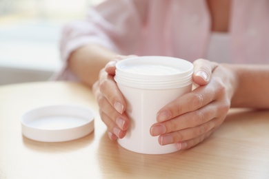 Photo of Woman with jar of moisturizing cream at table, closeup