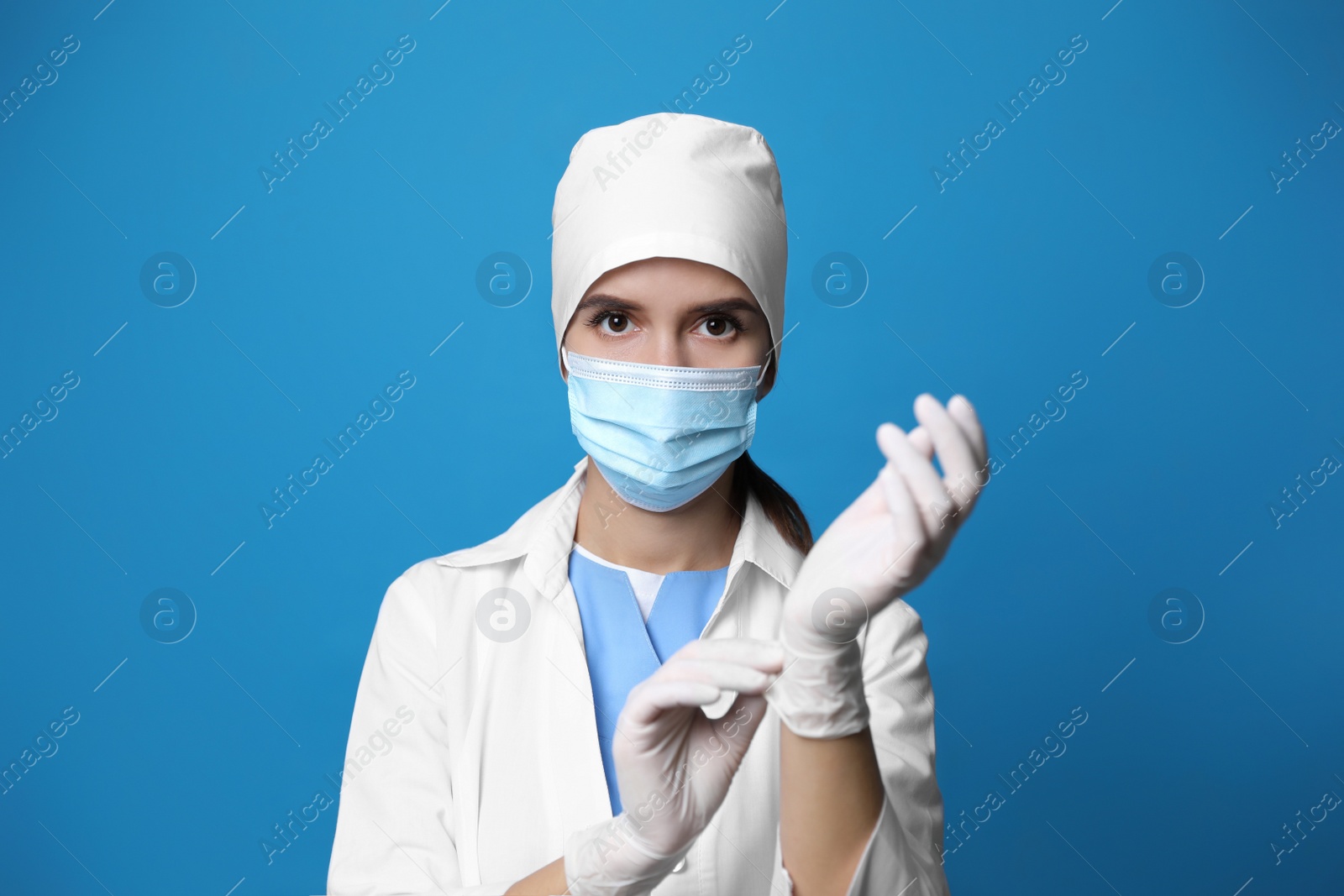 Photo of Doctor in protective mask putting on medical gloves against blue background