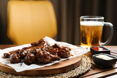 Photo of Tasty chicken wings, sauces and mug of beer on wooden table, space for text. Delicious snack