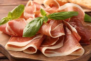 Photo of Slices of tasty cured ham and basil on wooden board, closeup