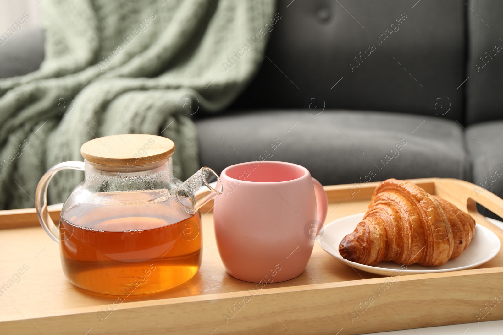 Photo of Aromatic tea in teapot, cup and tasty croissant on table indoors