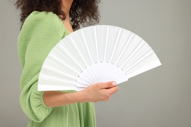 Woman holding hand fan on light grey background, closeup