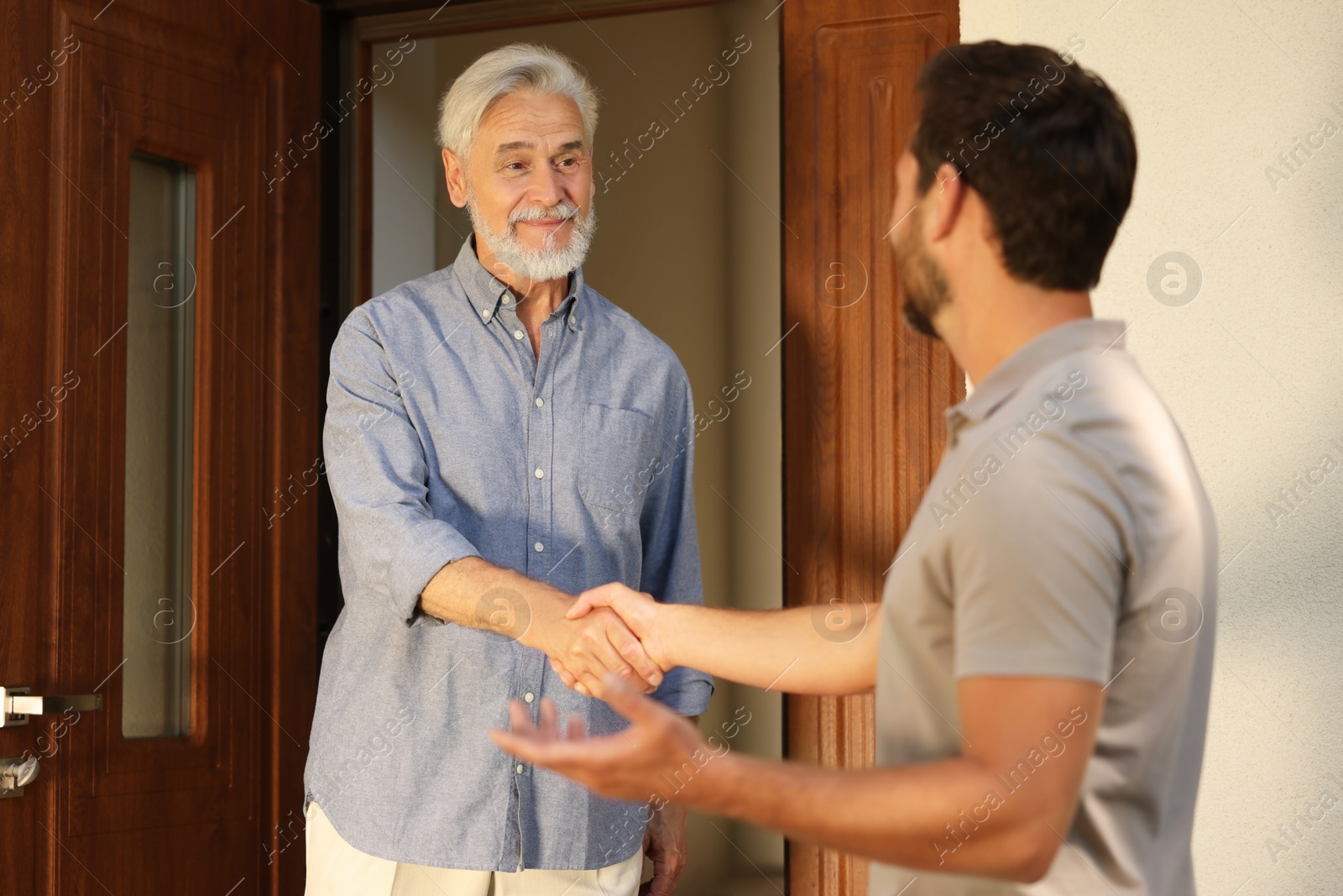 Photo of Friendly relationship with neighbours. Happy men shaking hands near house outdoors