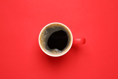 Cup of aromatic coffee on red background, top view