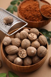 Photo of Nutmeg powder, seeds, grater and green leaves on light brown background