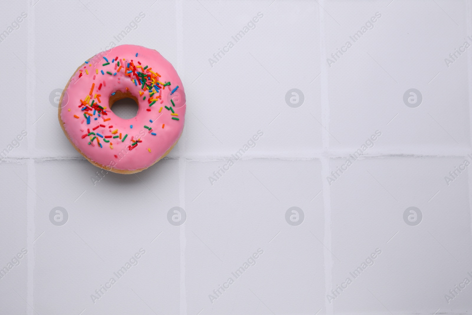Photo of Tasty glazed donut decorated with colorful sprinkles on white table, top view. Space for text