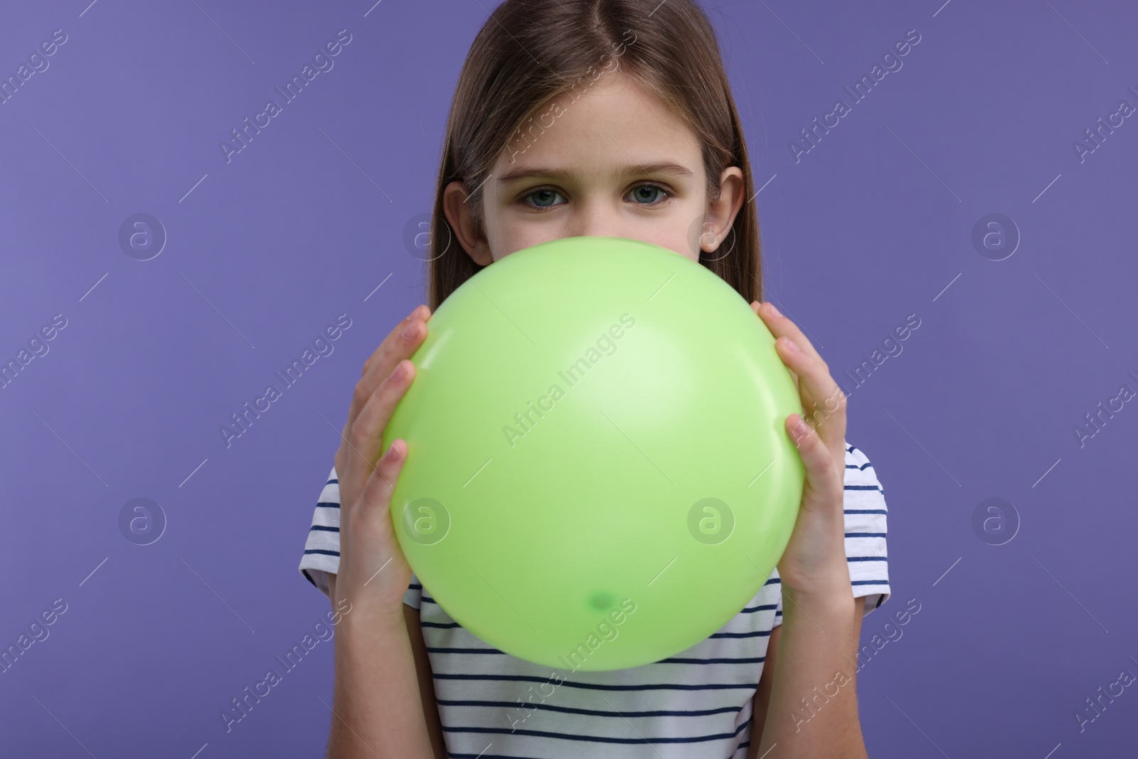 Photo of Girl inflating light green balloon on violet background
