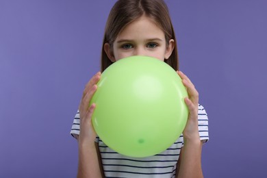 Girl inflating light green balloon on violet background