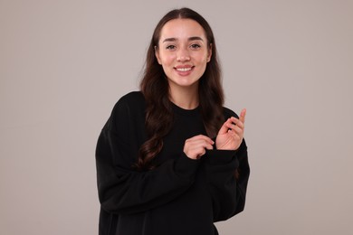 Beautiful young woman in stylish warm sweater on grey background