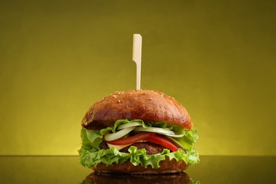 Photo of Delicious vegetarian burger on mirror surface against olive background