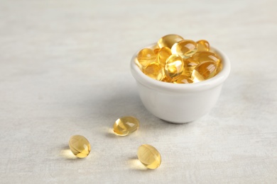Photo of Bowl with cod liver oil pills on light background