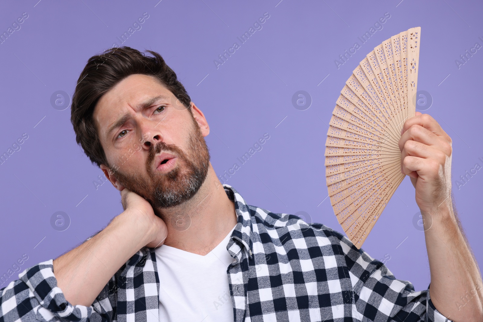 Photo of Unhappy man with hand fan suffering from heat on purple background