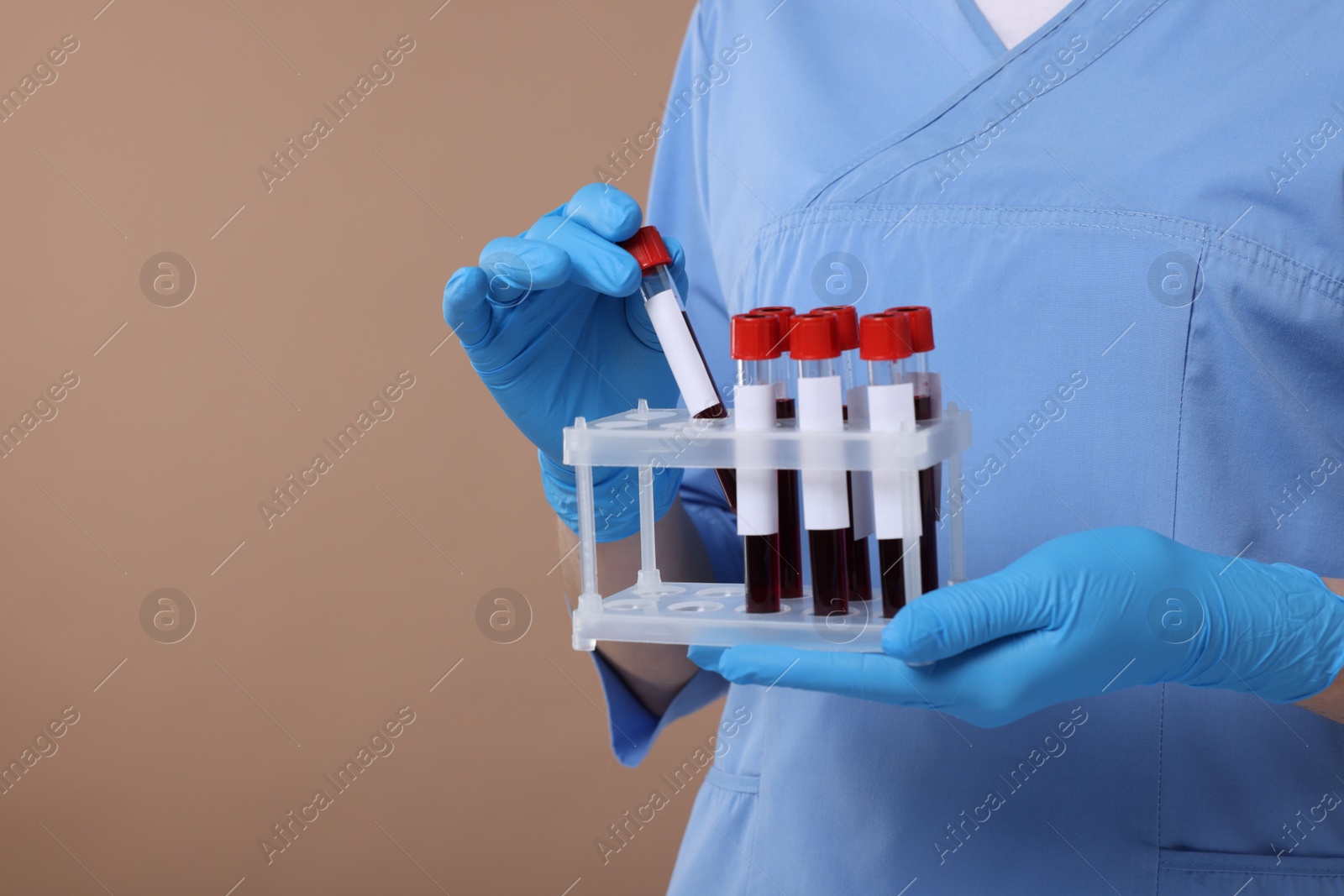 Photo of Laboratory testing. Doctor with blood samples in tubes on light brown background, space for text