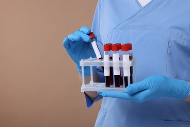 Laboratory testing. Doctor with blood samples in tubes on light brown background, space for text