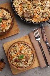 Photo of Delicious pilaf with meat and carrot served on grey textured table, flat lay