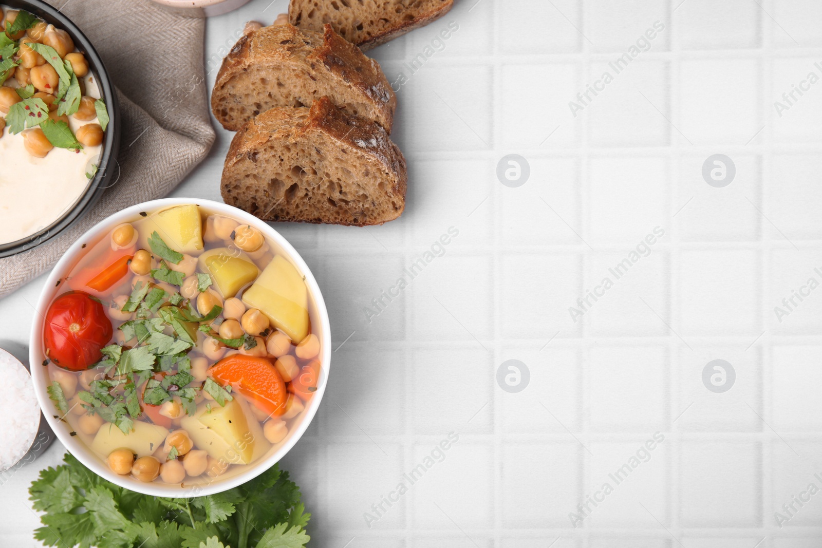 Photo of Flat lay composition of tasty chickpea soup in bowls, bread and parsley on white tiled table. Space for text